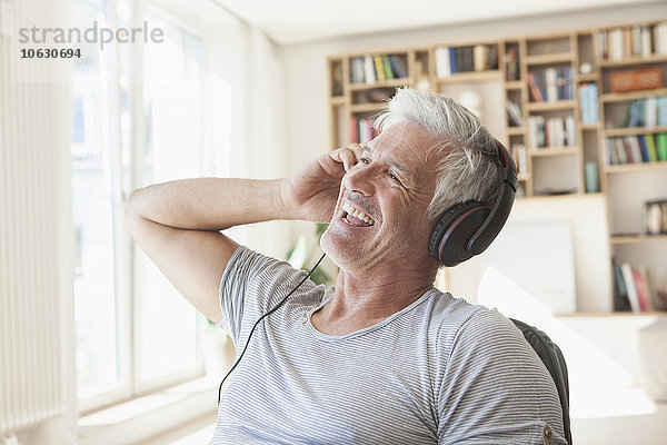 Porträt eines entspannten Mannes  der zu Hause Musik mit Kopfhörern hört.