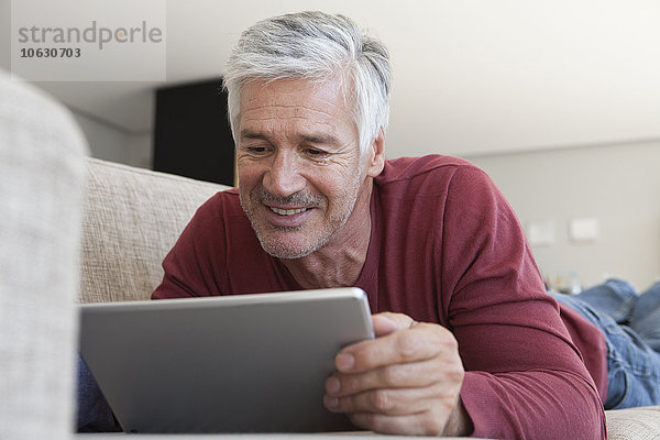 Porträt eines lächelnden Mannes  der zu Hause auf der Couch liegt  mit einem digitalen Tablett.