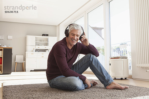 Porträt eines entspannten Mannes  der zu Hause auf dem Boden sitzt und Musik mit Kopfhörern hört.