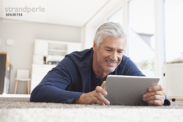 Lächelnder Mann zu Hause auf dem Boden liegend mit digitalem Tablett