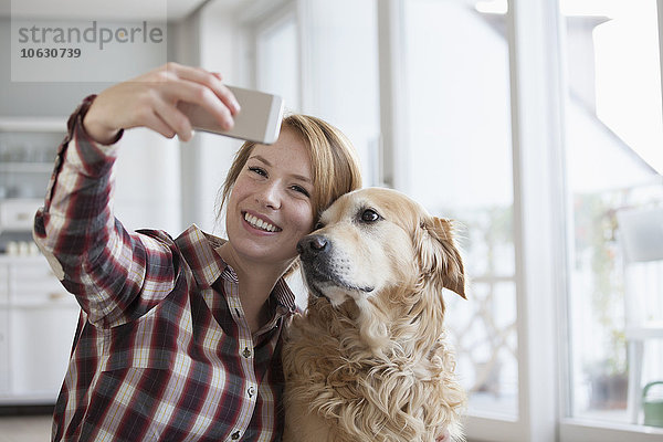 Porträt einer lächelnden jungen Frau  die einen Selfie mit ihrem Hund mitnimmt.
