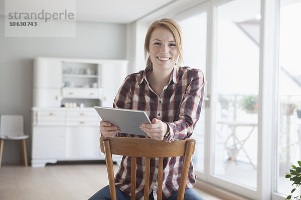 Porträt einer lächelnden jungen Frau mit ihrem digitalen Tablett zu Hause