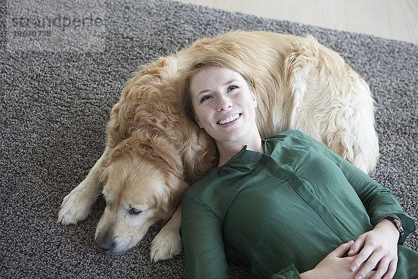 Lächelnde junge Frau entspannt mit ihrem Hund auf dem Teppich