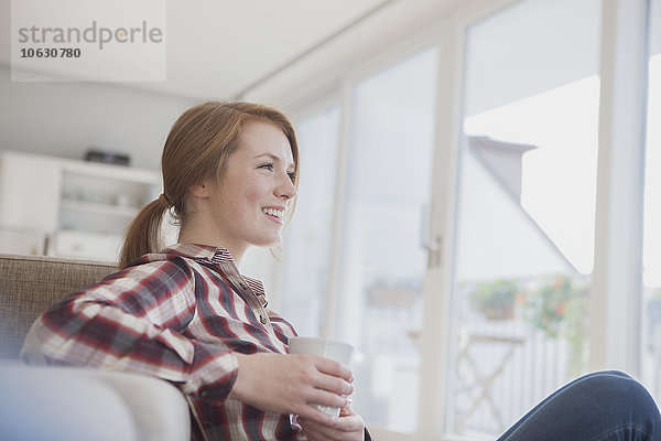 Lächelnde junge Frau entspannt bei einer Tasse Kaffee zu Hause