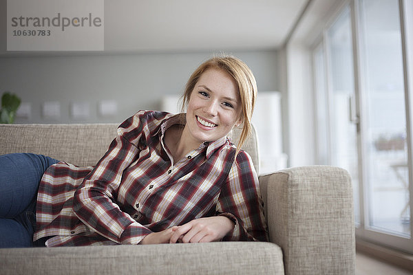 Porträt einer lächelnden jungen Frau  die zu Hause auf der Couch liegt.