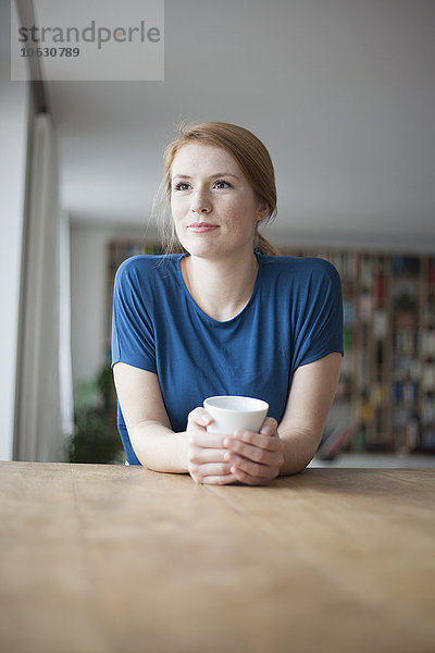 Porträt einer jungen Frau am Tisch sitzend mit einer Tasse Kaffee