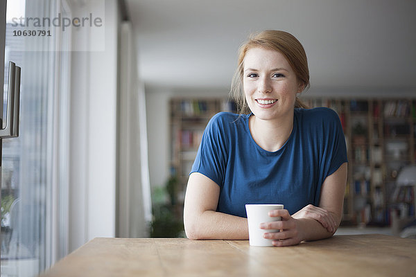 Porträt einer lächelnden jungen Frau am Tisch mit einer Tasse Kaffee