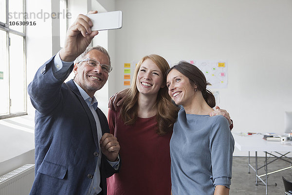 Lächelnder Geschäftsmann  der einen Selfie mit zwei Frauen im Amt hat.