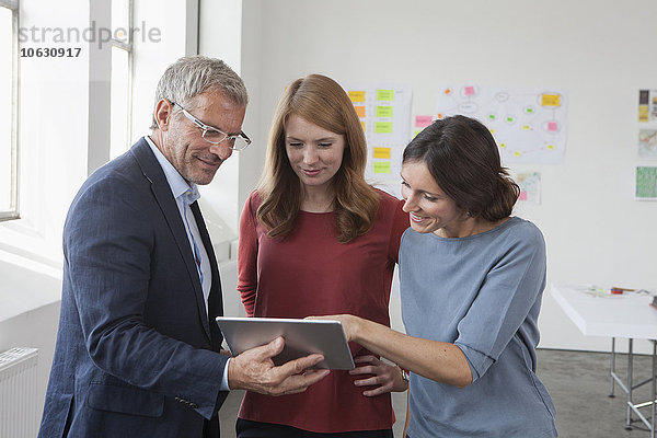 Lächelnder Usinessman und zwei Frauen im Büro beim Betrachten des digitalen Tabletts