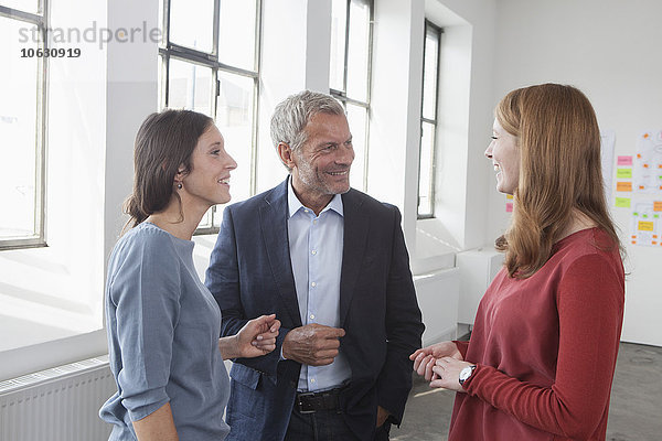 Lächelnder Geschäftsmann und zwei Frauen im Büro im Gespräch