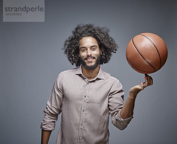Porträt eines lächelnden jungen Mannes mit lockigen braunen Haaren  der einen Basketball auf seinem Finger balanciert.