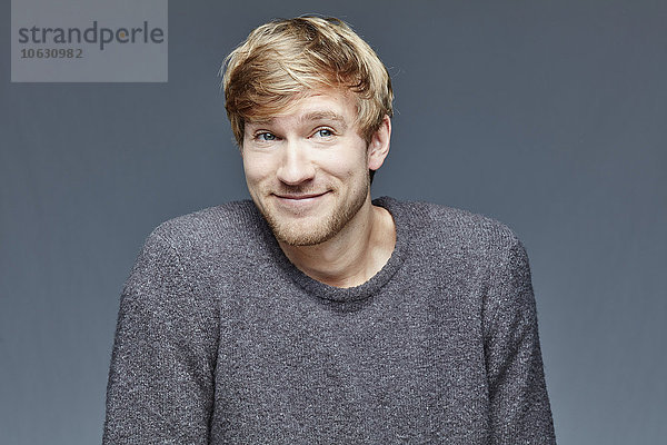 Porträt eines lächelnden blonden Mannes vor grauem Hintergrund