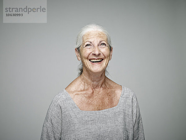 Porträt einer lachenden Seniorin  die vor grauem Hintergrund aufblickt