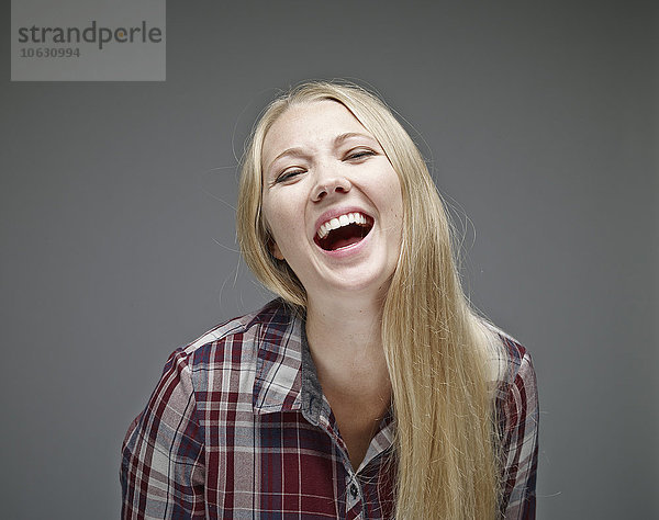 Porträt der lachenden jungen Frau vor grauem Hintergrund