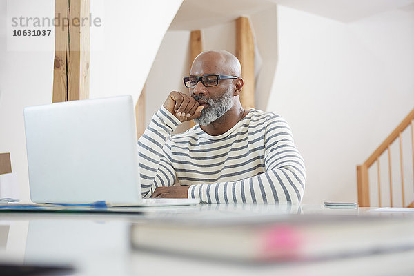 Porträt eines Mannes am Schreibtisch des Home Office mit Blick auf seinen Laptop