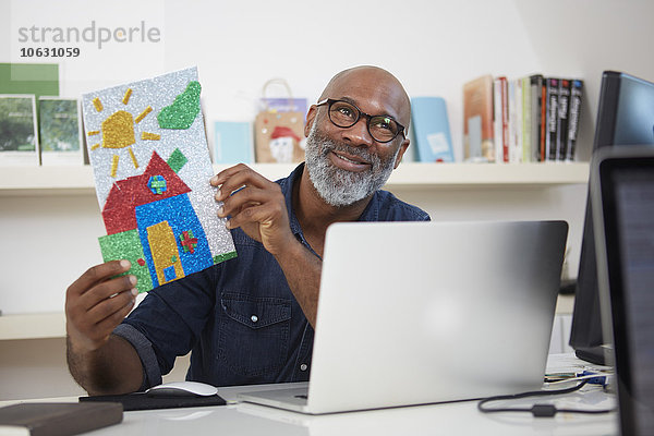 Porträt eines lächelnden Mannes am Schreibtisch mit Kinderzeichnung