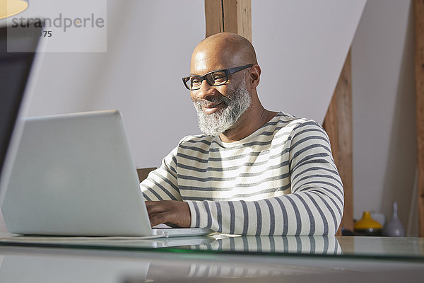 Portrait eines lächelnden Mannes  der am Schreibtisch sitzt und mit dem Laptop arbeitet.