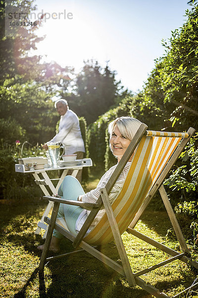 Reife Frau im Liegestuhl im Garten mit Mann im Hintergrund