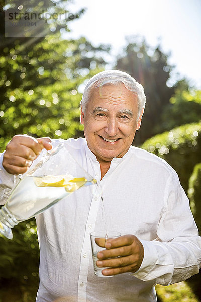 Lächelnder älterer Mann gießt Wasser ins Glas im Garten