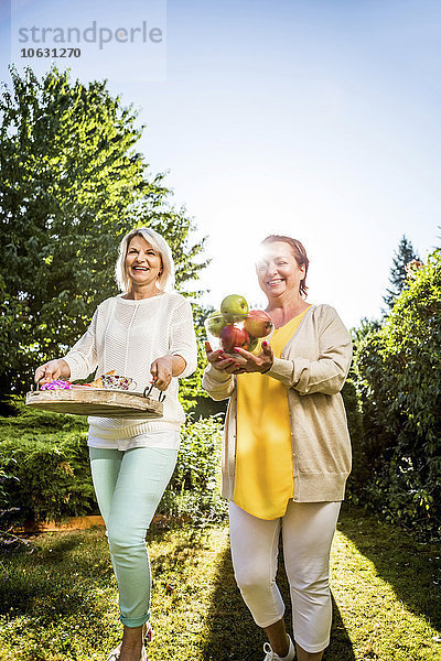 Zwei glückliche reife Frauen mit Äpfeln und Tablett im Garten