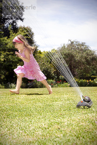 Kleines Mädchen spielt mit Rasensprenger im Garten