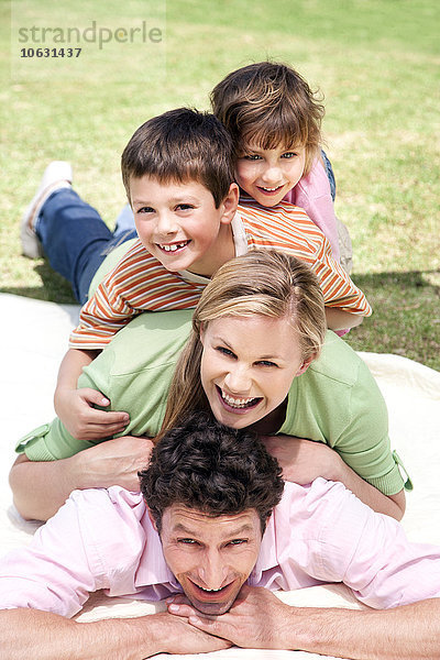 Gruppenbild einer glücklichen Familie  die übereinander auf einer Decke im Garten liegt.