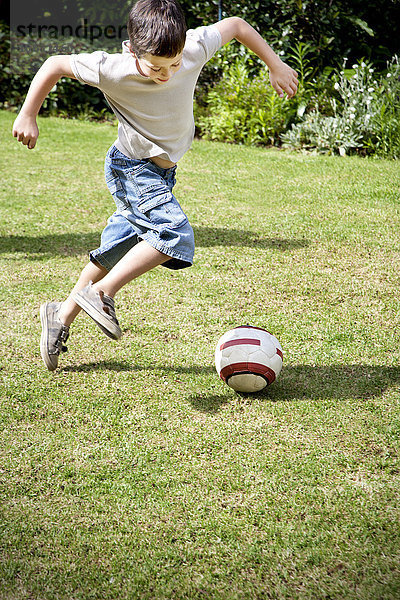 Kleiner Junge spielt Fußball im Garten