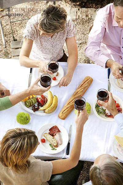 Spanien  Mallorca  fünf Freunde sitzen am gedeckten Tisch im Garten und rösten mit Rotwein.