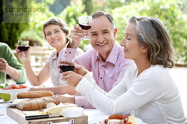 Spanien  Mallorca  reifer Mann sitzend mit Freunden am gedeckten Tisch im Garten  Toast mit Rotwein