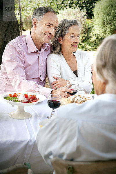 Porträt eines reifen Paares  das Seite an Seite am gedeckten Tisch im Garten sitzt.