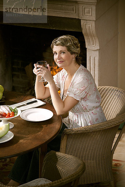 Porträt einer lächelnden reifen Frau  die am gedeckten Tisch sitzt und ein Glas Rotwein hält.