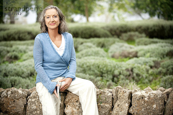 Spanien  Mallorca  Portrait einer reifen Frau  die auf einer Wand im Garten sitzt.