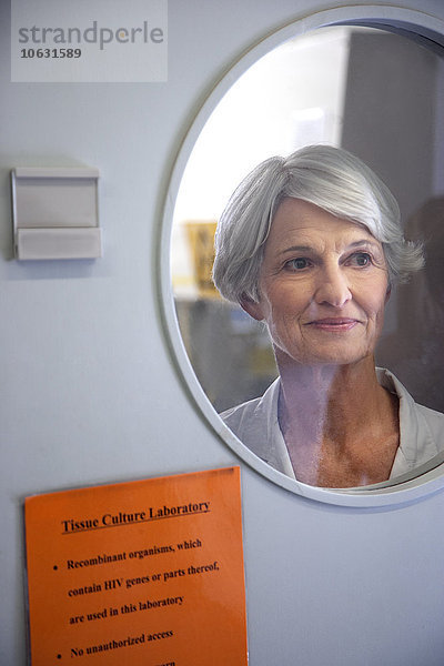 Seniorin schaut durch das Fenster der Labortür