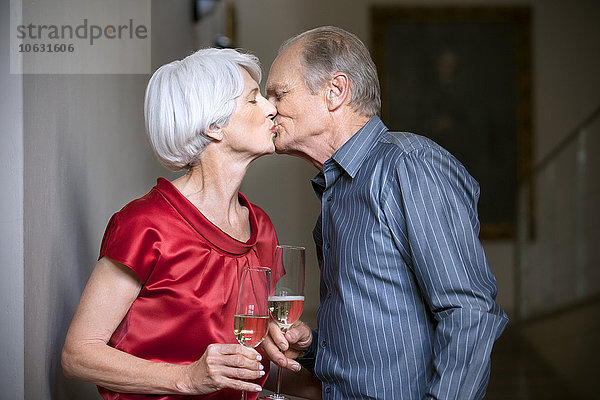 Seniorenpaar küsst und klirrt an den Gläsern