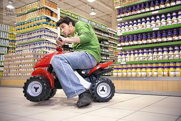 Mann fährt mit Spielzeugauto in einem Supermarkt