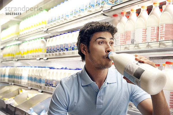 Mann trinkt Milch vor dem Kühlschrank im Supermarkt