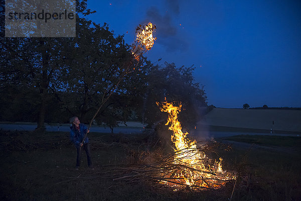 Deutschland  Junge am Lagerfeuer auf einer Wiese am Abend