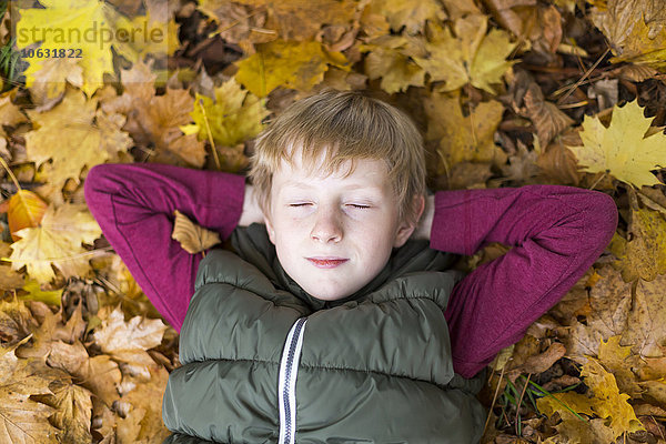 Porträt eines Jungen mit geschlossenen Augen  der sich auf Herbstblättern am Boden entspannt.