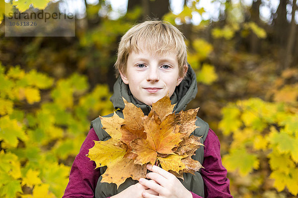 Porträt eines Jungen mit einem Haufen Herbstblätter
