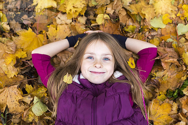 Porträt eines lächelnden Mädchens  das sich auf Herbstblättern am Boden ausruht