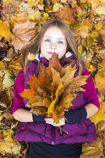 Porträt eines auf dem Boden liegenden Mädchens mit Herbstlaubbüschel