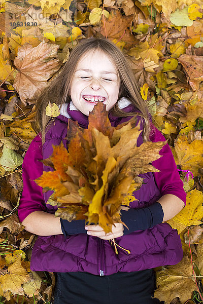 Porträt eines lachenden Mädchens  das auf dem Boden liegt und ein paar Herbstblätter hält.