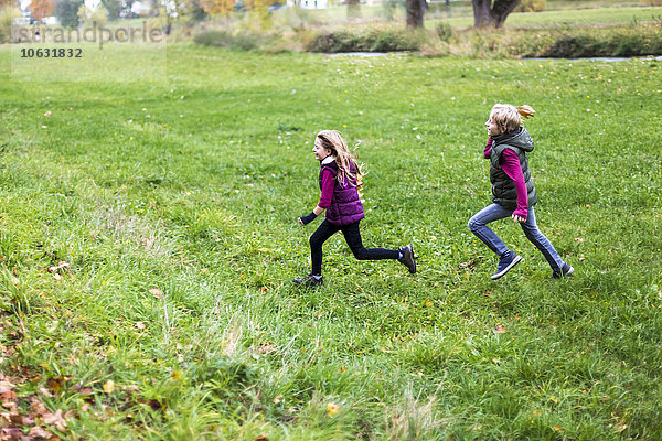 Junge und Mädchen rennen über eine Wiese.
