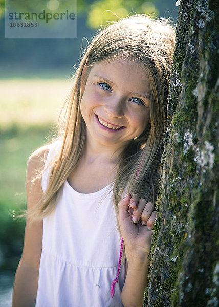 Porträt eines lächelnden kleinen Mädchens  das sich an einen Baumstamm lehnt.