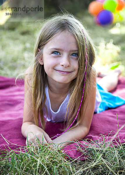Porträt eines lächelnden kleinen Mädchens  das auf einer Wiese auf einer Decke liegt.