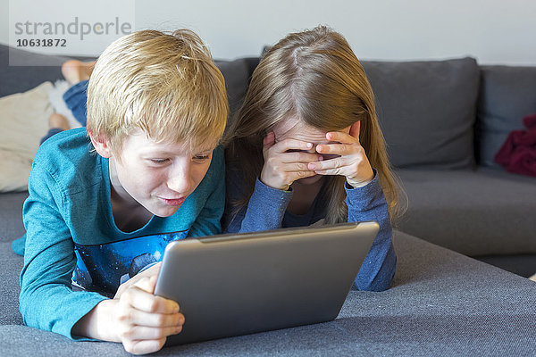 Junge und Mädchen auf der Couch liegend mit digitalem Tablett