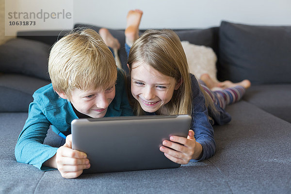 Junge und Mädchen liegen Seite an Seite auf der Couch mit digitalem Tablett