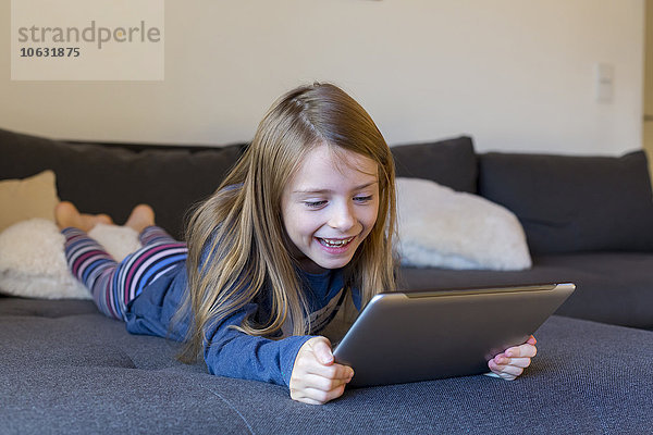 Lächelndes Mädchen auf der Couch liegend mit digitalem Tablett