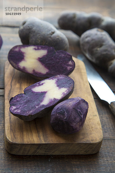 Geschnittene und ganze violette Kartoffeln auf Holzplatte