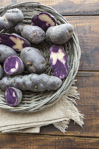 Geschnittene und ganze violette Kartoffeln in einem Weidenkorb